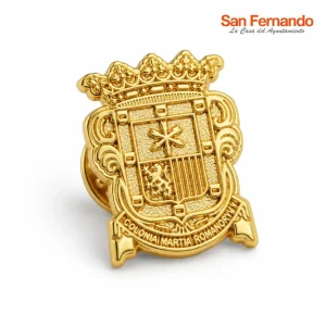 Pin institucional dorado para ayuntamiento con escudo heráldico, corona ornamental y detalles grabados en relieve.